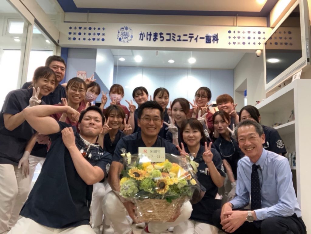 開院8周年のお祝いの花を囲むかけまちコミュニティー歯科のスタッフ一同